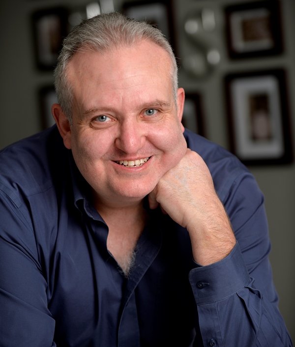 Portrait of a smiling grey haired man in a navy shirt resting his chin on his fist